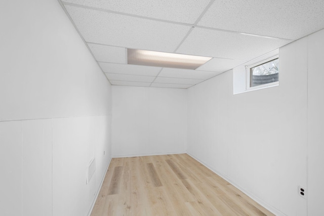 basement featuring light wood-type flooring, a paneled ceiling, and visible vents