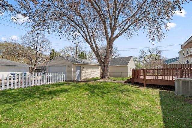 view of yard featuring a detached garage, a deck, fence, and an outbuilding