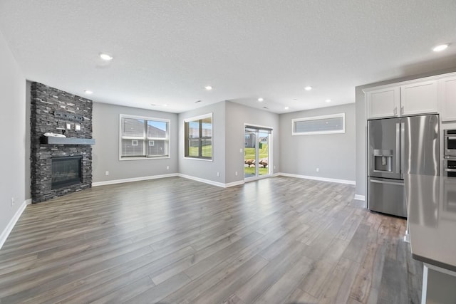 unfurnished living room with dark wood-type flooring, a textured ceiling, a fireplace, baseboards, and recessed lighting