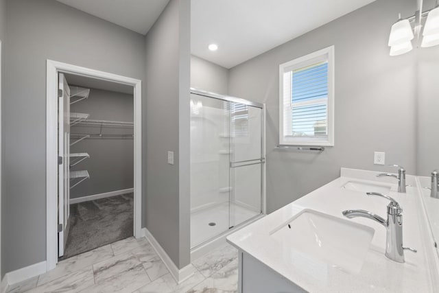 full bathroom featuring a stall shower, marble look tile flooring, baseboards, a spacious closet, and double vanity