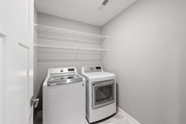 washroom with washing machine and dryer, light marble finish floors, and baseboards