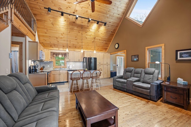 living room with light wood finished floors, high vaulted ceiling, rail lighting, plenty of natural light, and ceiling fan