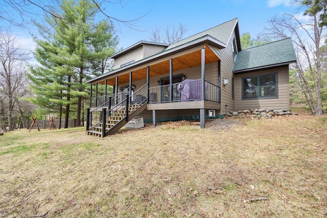 view of front facade featuring a shingled roof, covered porch, a front yard, and stairs