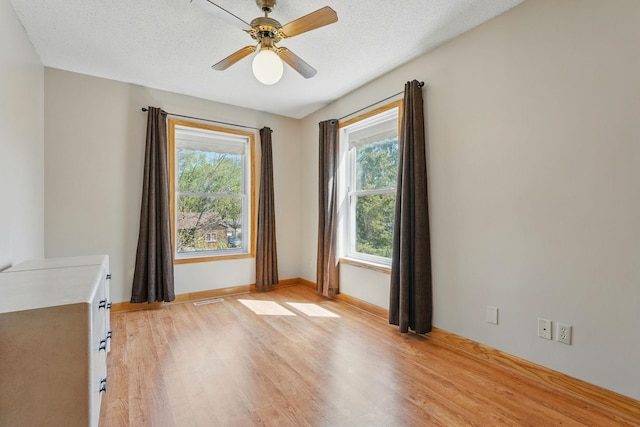 spare room featuring light wood finished floors, visible vents, baseboards, and ceiling fan
