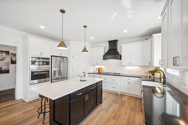 kitchen with premium range hood, stainless steel appliances, light wood finished floors, and a kitchen island
