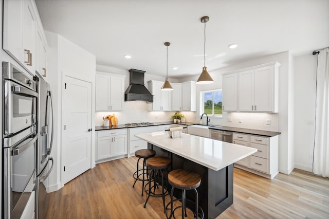 kitchen with tasteful backsplash, a sink, custom range hood, a kitchen bar, and appliances with stainless steel finishes