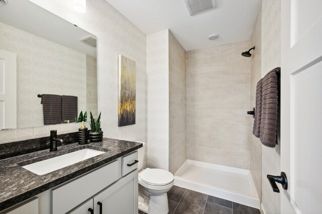 bathroom with a tile shower, tile patterned flooring, visible vents, toilet, and vanity