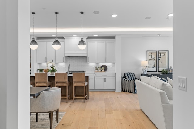 kitchen with decorative backsplash, a kitchen bar, decorative light fixtures, light wood-type flooring, and recessed lighting
