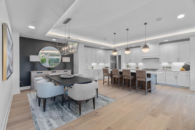 dining space featuring baseboards, a chandelier, a raised ceiling, and light wood-type flooring