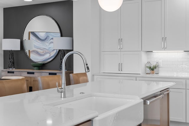 room details featuring a sink, decorative backsplash, light stone countertops, and white cabinetry
