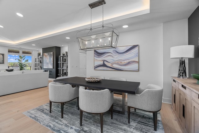 dining room with recessed lighting, a raised ceiling, light wood finished floors, and a notable chandelier