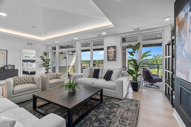 living area featuring recessed lighting, a tray ceiling, visible vents, and light wood-style flooring