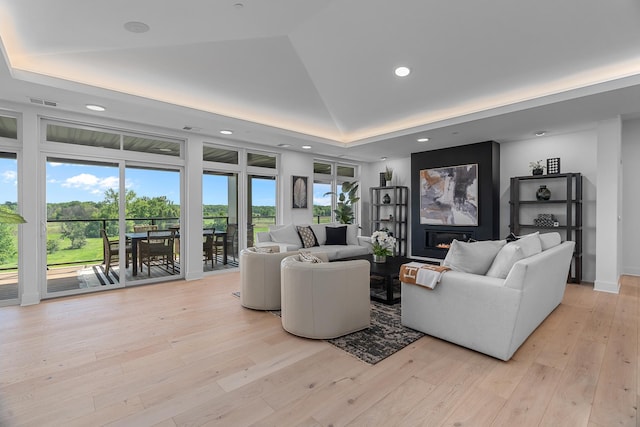 living room featuring recessed lighting, a tray ceiling, a glass covered fireplace, and light wood-style floors