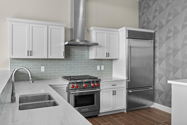 kitchen featuring high end appliances, light stone countertops, wall chimney exhaust hood, white cabinetry, and a sink