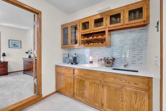 bar featuring light colored carpet, a sink, baseboards, and backsplash