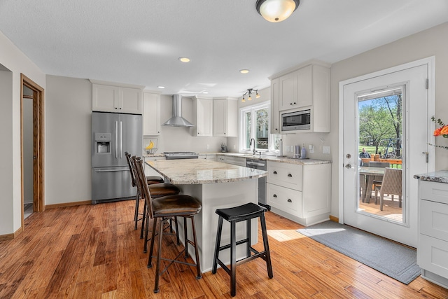 kitchen with wall chimney range hood, white cabinets, appliances with stainless steel finishes, and a breakfast bar