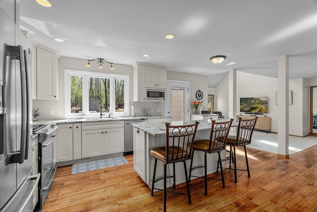 kitchen with a kitchen island, light wood-style floors, a kitchen breakfast bar, light stone counters, and stainless steel appliances