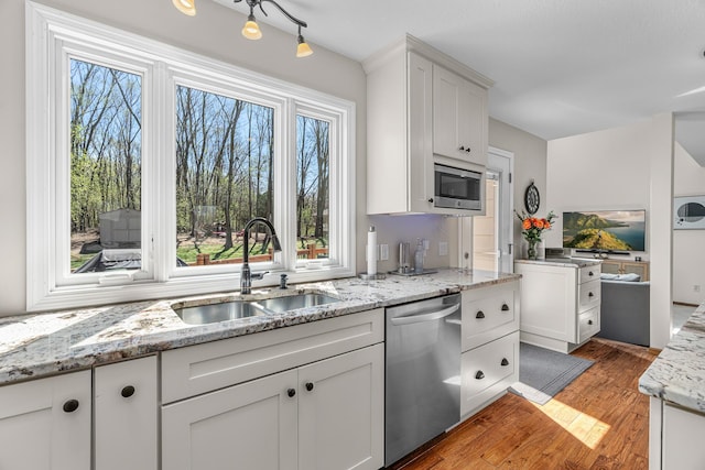 kitchen featuring light wood-type flooring, a sink, light stone counters, stainless steel appliances, and white cabinetry