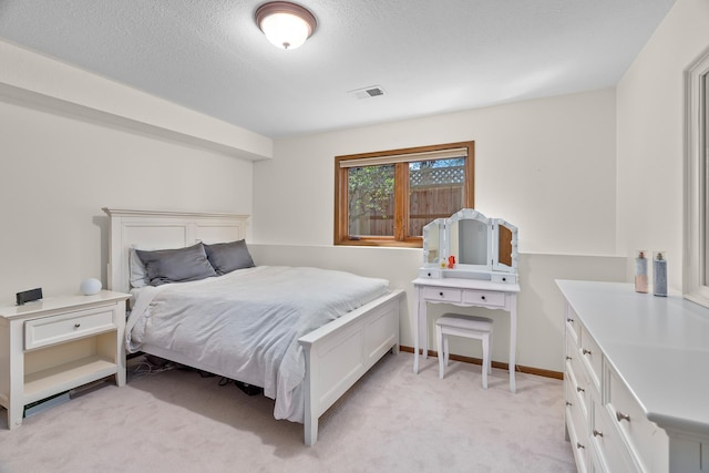 bedroom with baseboards, light carpet, a textured ceiling, and visible vents