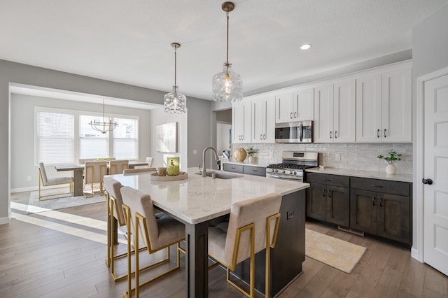 kitchen with a kitchen island with sink, hardwood / wood-style flooring, tasteful backsplash, a sink, and stainless steel appliances