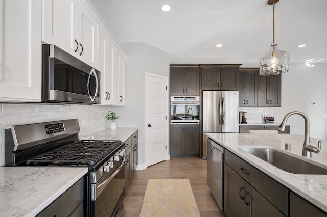 kitchen featuring wood finished floors, dark brown cabinetry, white cabinetry, a sink, and stainless steel appliances