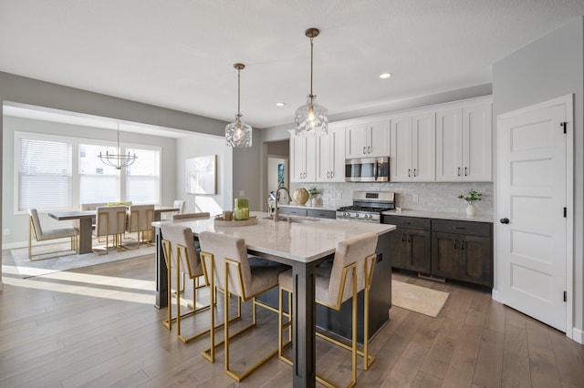 kitchen with a kitchen island with sink, appliances with stainless steel finishes, tasteful backsplash, a sink, and a chandelier