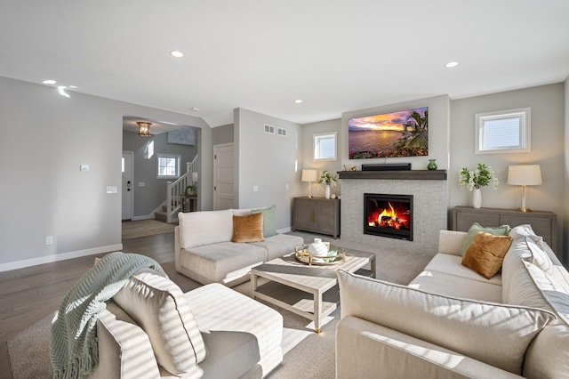 living room with stairs, a glass covered fireplace, wood finished floors, baseboards, and recessed lighting
