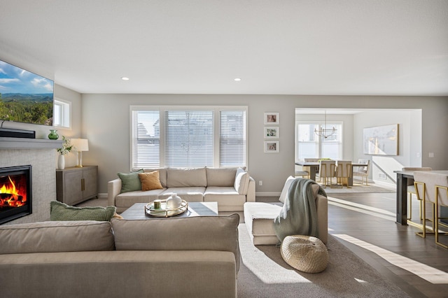 living area featuring baseboards, a glass covered fireplace, dark wood-style floors, an inviting chandelier, and recessed lighting