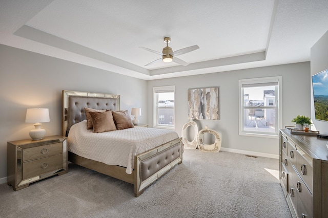 bedroom with ceiling fan, light carpet, baseboards, a tray ceiling, and visible vents
