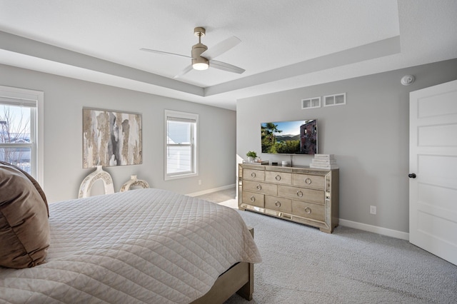 bedroom with a tray ceiling, visible vents, light carpet, and baseboards