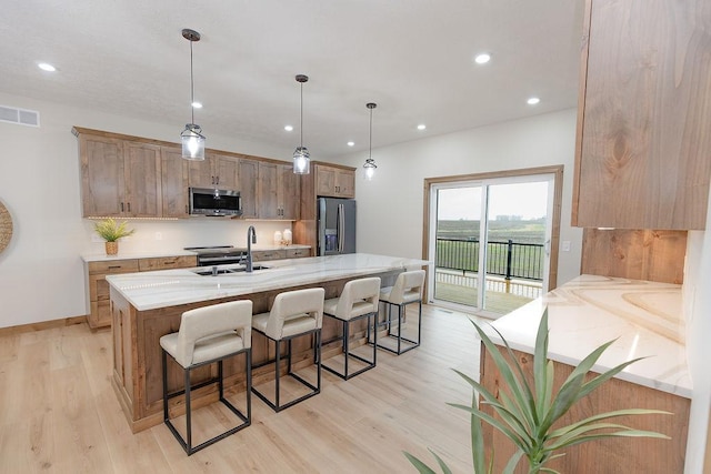 kitchen with visible vents, light wood-type flooring, a large island with sink, a sink, and appliances with stainless steel finishes