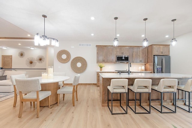 kitchen featuring a kitchen bar, visible vents, light wood-style floors, stainless steel appliances, and an island with sink