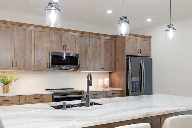 kitchen featuring stainless steel microwave, hanging light fixtures, black fridge, and light stone counters