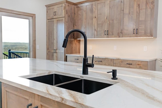 kitchen featuring light stone countertops, a sink, and light brown cabinets