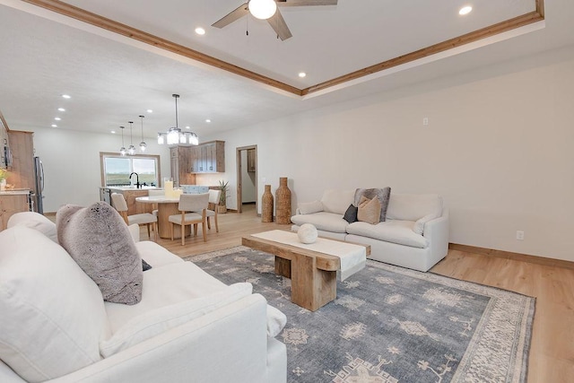 living room featuring baseboards, ceiling fan with notable chandelier, ornamental molding, recessed lighting, and light wood-style flooring
