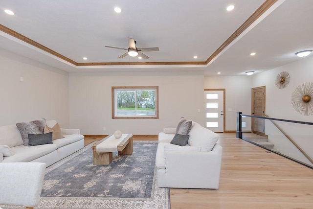 living room featuring crown molding, recessed lighting, a raised ceiling, and light wood-style floors
