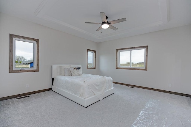 bedroom with carpet flooring, a raised ceiling, a ceiling fan, baseboards, and visible vents