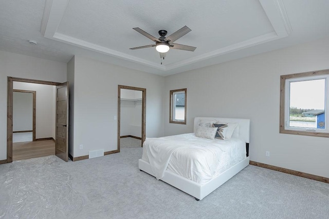 carpeted bedroom featuring visible vents, a raised ceiling, baseboards, and multiple windows