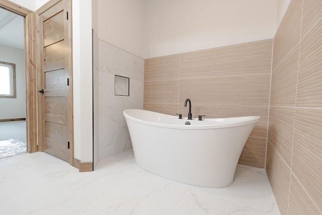 full bathroom featuring marble finish floor, a freestanding tub, and tile walls