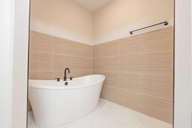 bathroom with marble finish floor, a freestanding bath, and tile walls
