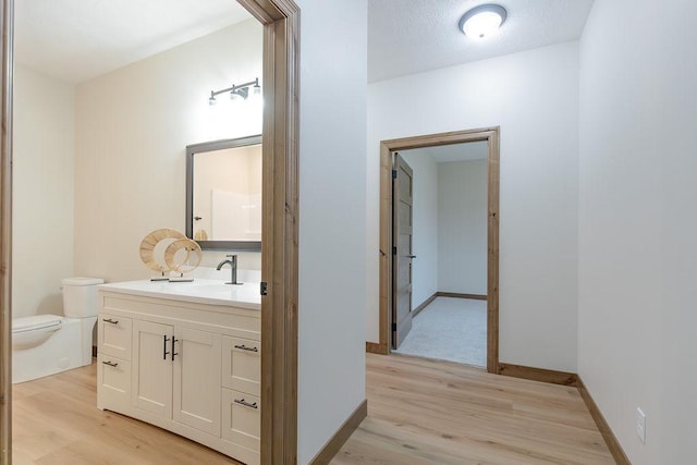 half bath with vanity, baseboards, wood finished floors, and toilet
