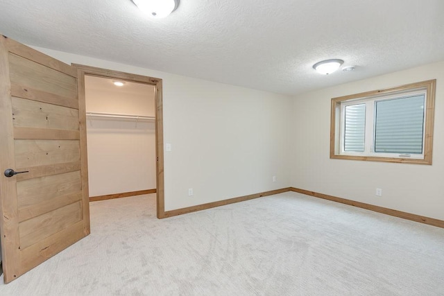 unfurnished bedroom featuring a textured ceiling, a spacious closet, light carpet, and baseboards