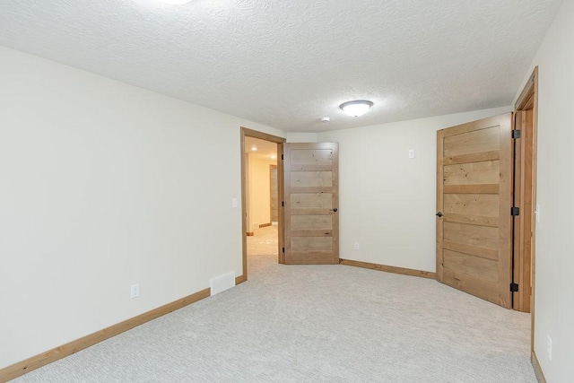 spare room featuring a textured ceiling, baseboards, visible vents, and carpet