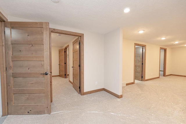 interior space featuring baseboards, recessed lighting, a textured ceiling, and light carpet