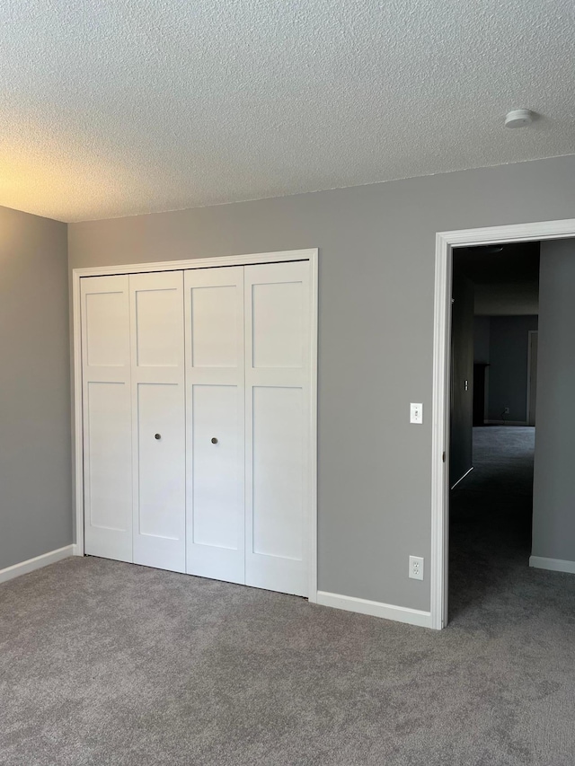 unfurnished bedroom featuring carpet flooring, a closet, a textured ceiling, and baseboards