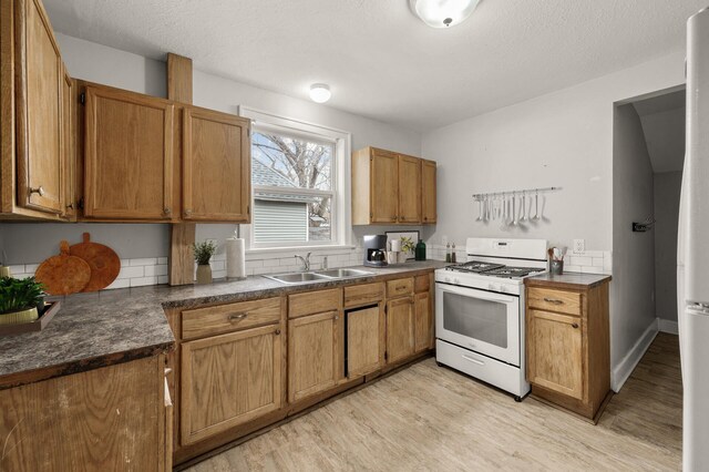 kitchen featuring brown cabinetry, dark countertops, white gas stove, light wood-type flooring, and a sink