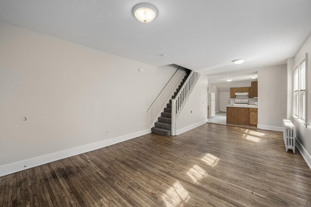 unfurnished living room featuring baseboards, stairs, radiator heating unit, and dark wood finished floors