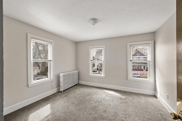 carpeted spare room featuring a textured ceiling, baseboards, and radiator