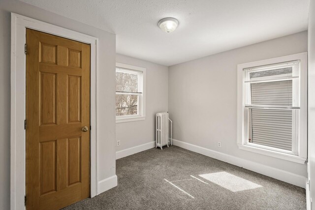 carpeted empty room with radiator and baseboards