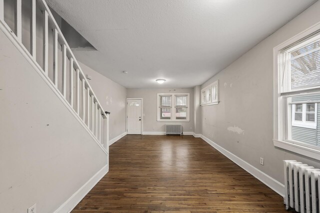 foyer entrance with baseboards, radiator, dark wood finished floors, and stairway